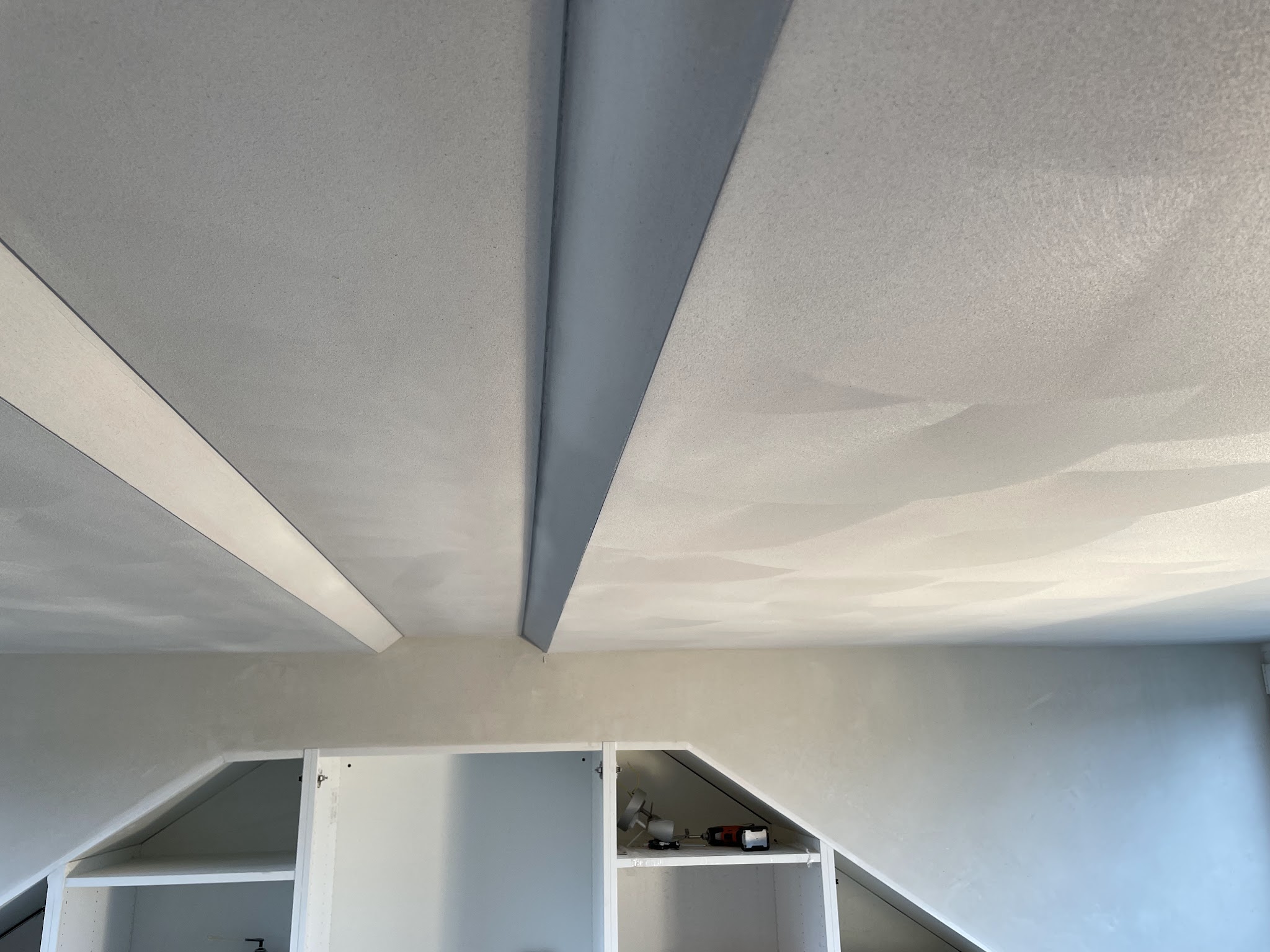 Gestuct plafond en schuine wanden boven witte inbouwkasten